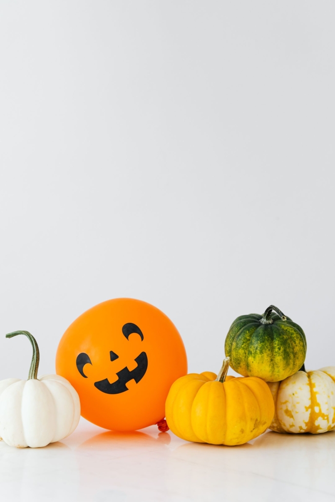 Globo de látex naranja con cara de calabaza junto a calabazas de verdad